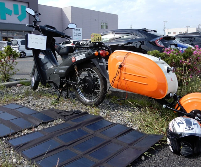 都市部ではソーラーパネルを広げて充電できる場所を探すのがとにかく大変。バイクに電話番号を書いたホワイトボードをつるしておく