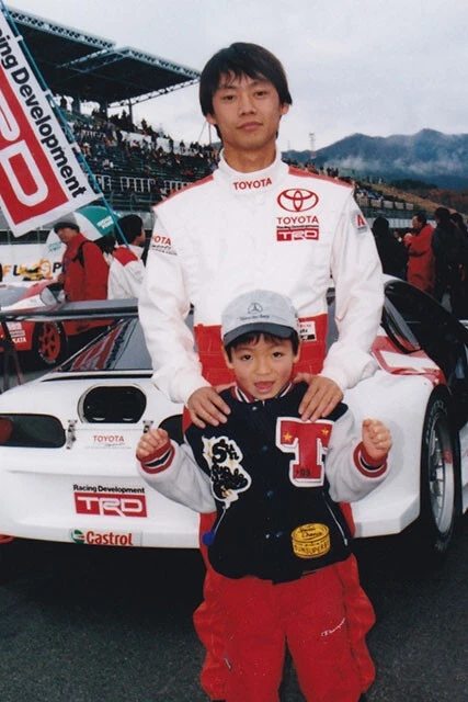 モータースポーツ好きの父に連れられ、幼い頃からレース会場に足を運んでいた。後ろは＂ミスターGT＂ことレーサーの脇阪寿一氏