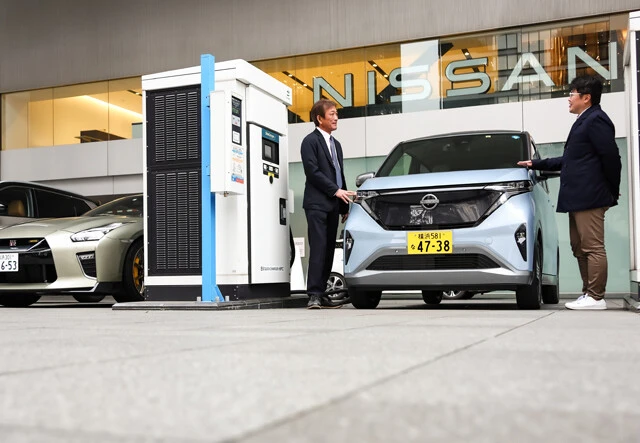 日産グローバル本社前にある充電スタンドに滑り込んだサクラを挟み、永井氏(左)に話を聞く山本氏(右)