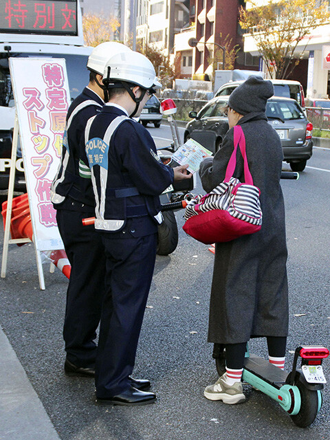 電動キックボード利用者に対し、安全運転の徹底を呼びかけるチラシを配布する警視庁の警察官。多くの利用者はヘルメット未着用