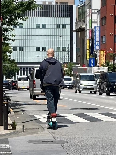 ノーヘルで車道を走行する電動キックボード利用者。都内の四輪ドライバーからは「ヘルメット姿をほとんど見かけない」との声が多い