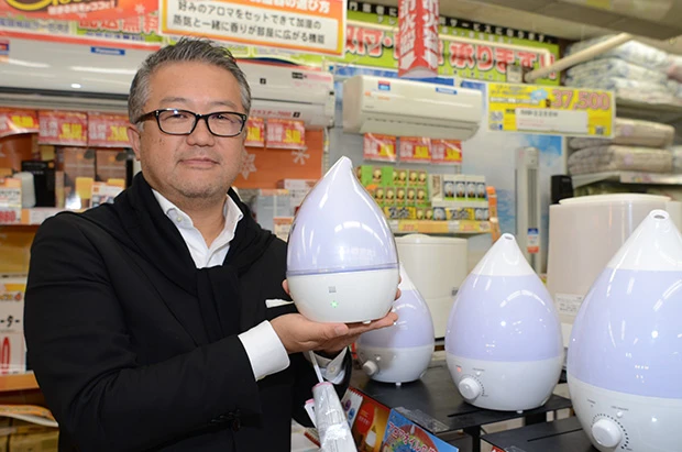 最新の七色に光る超音波加湿器「レインボーデュープレミアム」を手に持つ小田切氏。独特な光の使い方も「情熱価格」の特徴だ