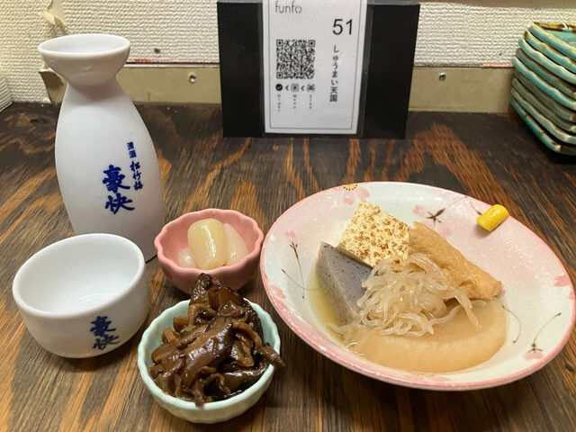 「中トロと豚足」で1円日本酒を一献。つまみは花らっきょ（9円）、しいたけ煮（9円）、おでん盛り合わせ（99円）。これ全部で会計は税込130円でした……