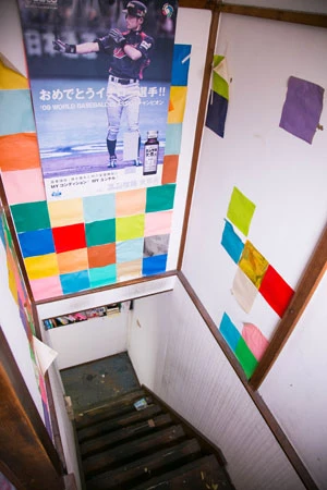 会場の2階へ続く階段もカラフル。家中、原色に囲まれて生活していたのだ。イチローのポスターが時代を感じさせる