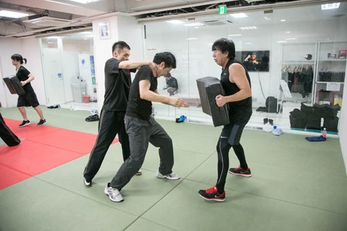ふたりに襲われたときの対処を交代で学ぶ。写真で岡村氏(右)はパッドを抱えているが、このときメインで練習している中央の受講者を前から襲っている役割だ。味方(左)が後方から攻撃しているときが、ほんの少しだけ体力回復のチャンス