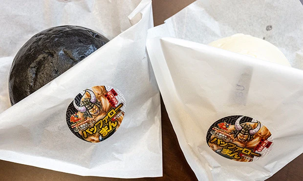 白い皮は牛肉と玉ねぎを詰めた本格派、黒い皮は牛肉・牛スジを入れて七味を利かせたワイルド派。2種類の肉まんで正義と悪魔に揺れ動くバッファローマンを表現。価格:各481円(税込、白・黒各1点)※各日販売予定70点