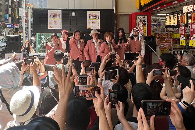 7月30日にMEGAドン・キホーテ渋谷本店の入り口にある水槽の前で開催されたリリースイベントの様子。ファンはもちろんのこと、たまたま通りかかった外国人観光客も彼らのアツい演奏に立ち止まり、にぎやかなアッパーチューンにノッていた。8月にはドン・キホーテ横浜西口店でもリリースイベントを開催予定