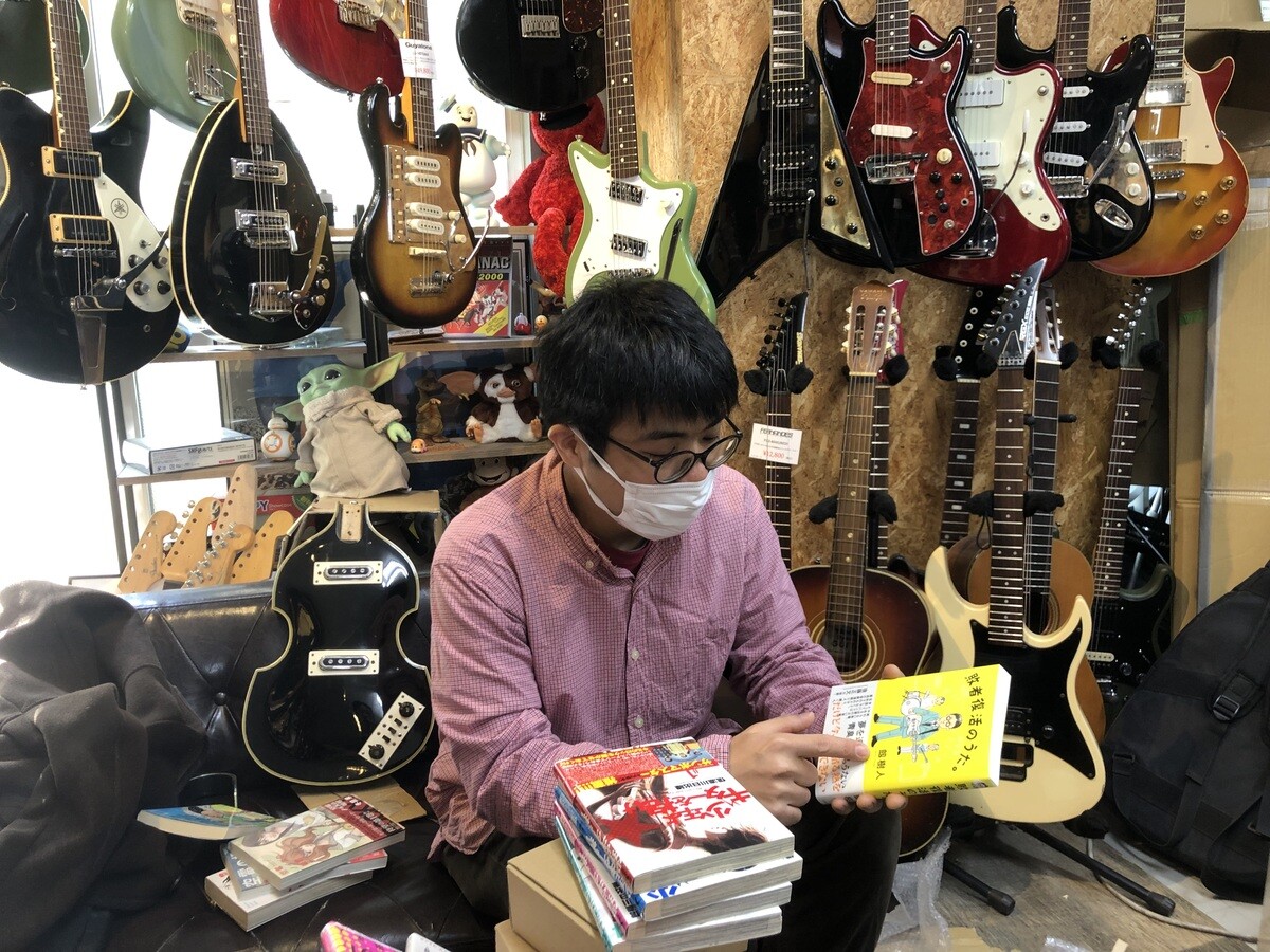 バンド漫画コレクターにしてバンド・トリプルファイヤーのベーシスト、山本慶幸さん。自身が働くギター工房「Astronauts Guitars」にはギターとバンド漫画であふれかえっている