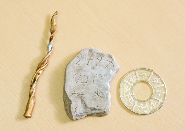 写真④ 中野氏の作った人工世界で用いられるアイテムで、左からペン軸、石板、護符。いずれにもヴァロケリム語やアルティジハーク語などの人工言語の文が刻まれている