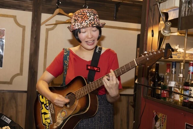 サムカワ氏のギターストラップに付いている、文字が流れるバッジが協会員の証。これがないパフォーマーとはトラブルが起きても流し協会は関与しません！