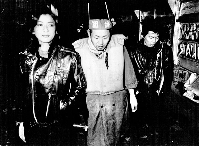 泉谷（中央）が美術監督を担当、俳優としても出演した伝説的映画『爆裂都市 BURST CITY』の撮影現場で。泉谷の左隣にいるのは、見学に訪れていたところ、急遽カメオ出演することになった関根恵子（現高橋惠子）