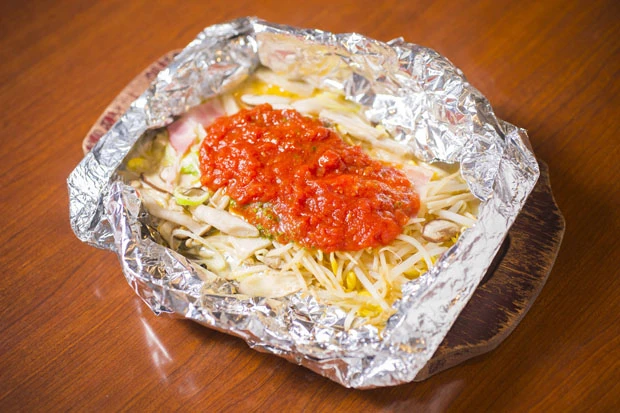 もやし、きのこ、ベーコン、チーズ、トマトソースが入ったホイル焼き。ホイルを破ると熱々の湯気が一気に上がり、目にもおいしい