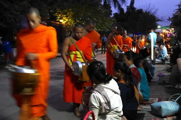 女性はひざまずき、男性は立ったままで、もち米、バナナ、おせんべいなどを喜捨し手を合わせる。僧のスピードの速さに写真はブレてるのばっかり(笑)