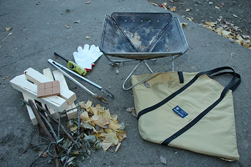 落ち葉、薪、着火具、着火剤、焚き火台、軍手、トング。軍手や火バサミがあると、安全に炎を扱える。