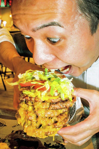 チャレンジする記者。パティは脂肪分20%以下の赤身から作られるため、想像以上にヘルシー。完食すると店内に記念写真が張られ、認定証が進呈される