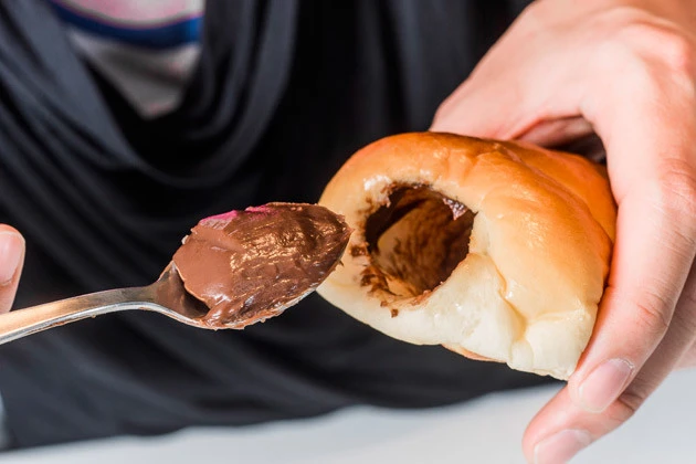 (1)抜く! コロネを焼くところから作るのは大変なので、市販のチョココロネを用意。スプーンを使って中身に詰まったチョコを抜いていく。気分は「池の水ぜんぶ抜く大作戦」だ