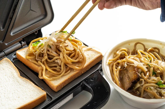 (1)のせる! ホットサンドメーカーに食パンをのせ、その上に豚ラーメンの麺と野菜をたっぷりのせる。さらに焼き豚切り落しもマシマシし、豚ラーメンのスープを大さじ1杯程度かけよう