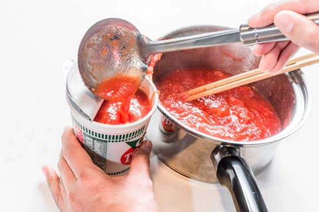 (2)注ぐ! チリトマトヌードルの容器を軽く押しつぶし、麺を軽く砕いてからトマトを注いでいこう。麺を砕かないとトマトが底まで浸透せず、すぐにあふれてしまうので気をつけよう