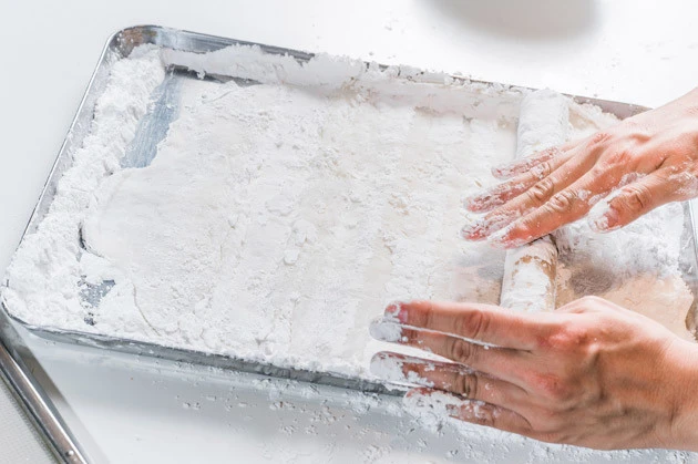 (2)延ばす! コーンスターチを敷いた台の上にレンチンしたモチを広げ、全体にコーンスターチをまぶしながら薄く延ばしていく。粉が少ないとモチが台にくっつくので要注意