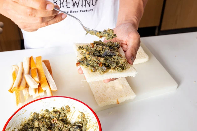 (3)のせる! 食パンの耳を切り落とし、中央に具をたっぷりのせる。その上から食パンをもう1枚のせ、包丁で半分にカットして盛りつけたら「悪魔のブラックたまごサンド」の完成!