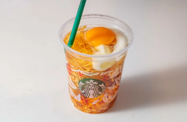 （３）入れる！　麺の上に卵を割り、そのままカップに熱湯を注ぎ、フタをして３分待つ。今回は平気だったが、アイスコーヒーのカップで作る場合はカップが溶けないよう湯温に気をつけるべし