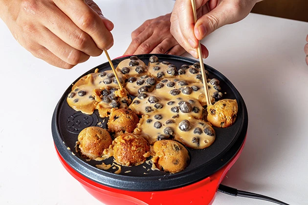 (3)焼く! 熱したたこ焼き器にバターを塗ってから生地を流し入れ、たこ焼きを焼く要領で焼き上げる。バターは高級品だが多めに使うほど風味が増す上に表面がカリッと仕上がる