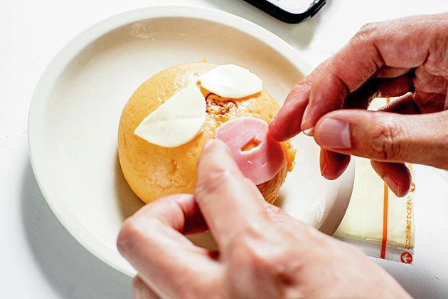 (3)デコる! キャラ弁を作る要領で表面にキン肉マンの顔を作ろう。目にはスライスチーズ、口はハムをベースに、きざみのりを使って線を描き、鼻や頭は裏面の皮を少しちぎって使用する