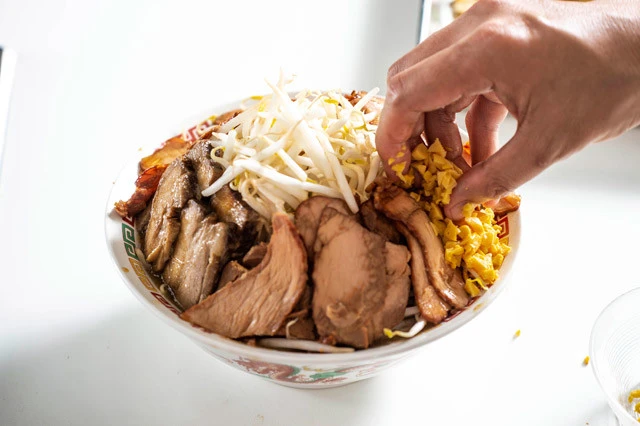 トッピングで完成度アップ! 大きめの丼に麺とスープを盛りつけ、野菜、ニンニク、豚肉をマシマシでトッピング。ひととおりセブンで購入できるため、普段豚ラーメンを食べるときにもぜひ利用したい。これに二郎の一部店舗で提供される納豆を追加することで、より濃厚な味わいを楽しめる