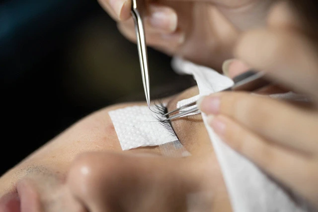 目のまわりをテープで保護し、まつげに接着剤をつけてピンセットで１本１本丁寧につけていく。所要時間は左右２０本ずつの場合、約６０分