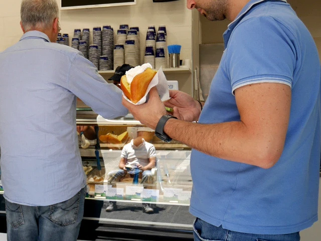 「ブリオッシュ・コン・ジェラート」を楽しむ青シャツの男たち。ブリオッシュとは、シチリアではふわふわしたほんのり甘いパンのこと。ジェラートをたっぷり挟んでいただくのがシチリア流