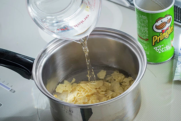 (1)煮込む! 粉々に砕いたプリングルズを鍋に入れ、全体が浸るくらいの量の水を注ぐ。全体がしんなりと柔らかくなるまで中火で煮込む。焦げつかないように時々かき混ぜよう