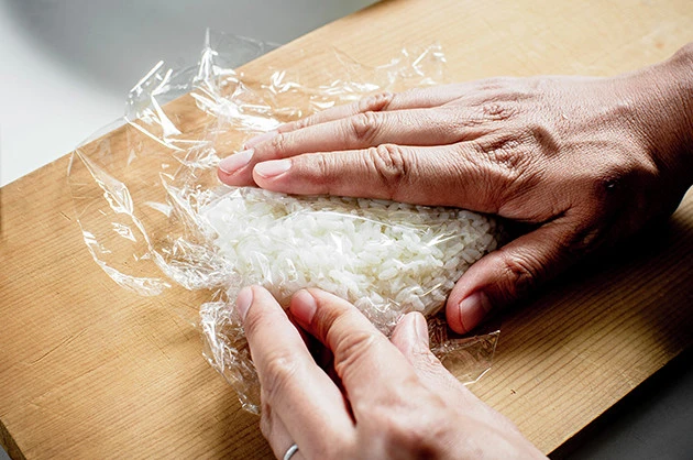 (1)握る! 軽く湿らせたご飯をまな板の上にのせ、ラップを使って全体を握りながら豚ロース肉の形に整える。「これは米ではない。豚だ!」と思い込みながら握ることが重要だ
