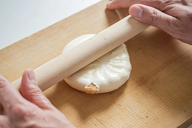 (2)延ばす! 肉まんをまな板の上に移し、麺棒を使って肉まんを平べったく広げていく。強く押しすぎると中身が飛び出るので注意。棒に生地がくっつく場合は少し生地を湿らせよう