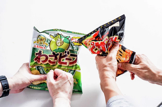 (1)砕く! わさビーフとピザポテトの袋をそれぞれほんの少しだけ開けて空気穴を作り、全体を豪快に揉みほぐしてポテチを砕く。粉々にはしすぎず、1cm角ほどの大きさを目標にしよう