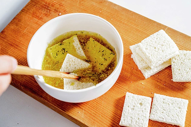 （２）吸収！　サンドイッチ用のパンを６等分にカットし、溶かしたガーリックマーガリンを極限まで吸収させる。耳を落とした食パンでも代用可能だが、８枚切りなどの薄いものを使用しよう