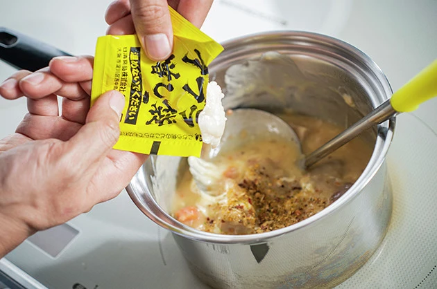 (3)味つけ! オニオンガーリックスパイスと豚ラ王のアブラ増し袋も入れ、よくかき混ぜながらさらに煮込んだら完成。シュクメルリ鍋は熱さも重要。すぐに食器に盛りつけよう