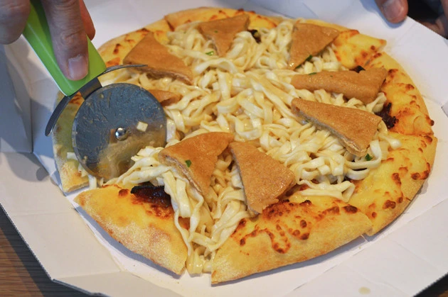 (4)カット! ピザカッターを用意し、ピザがもともとカットされている位置に合わせてどん兵衛の麺もカットする。あとは麺とお揚げを包むようにピザ生地を手に取って一気にかぶりつこう