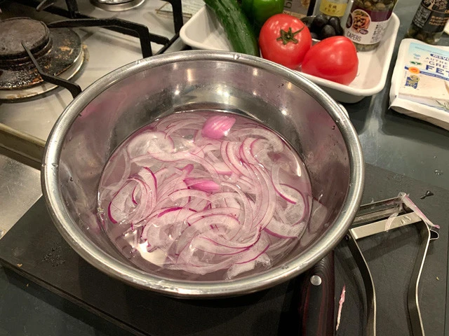 １．赤玉ねぎをスライサーやピーラーなどで薄切りにし、ボウルに入れ水につけておく。大さじ１程度の酢（分量外）を入れると赤玉ねぎの辛味が抜けやすい。