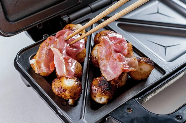 (1)並べる! 串から外した団子をホットサンドメーカーに隙間なく並べ、その上にあらかじめフライパンで焼いておいたベーコンをのせる。団子が固い場合は事前にレンチンで解決