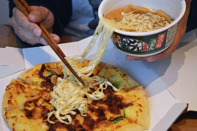 (3)ぶっかけ! ドミノ・ピザの高麗カルビを開封し、どん兵衛の麺を豪快にピザの上からぶっかけよう。つゆは麺に絡みついている分だけでOK。仕上げにお揚げを均等に並べよう