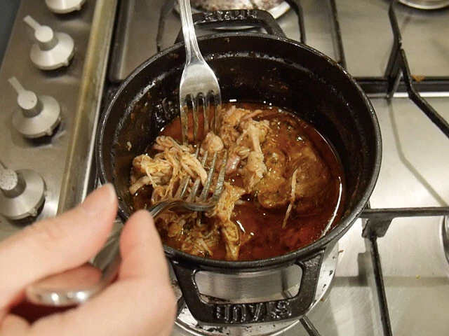 ３．煮込まれた肉をフォーク２本で細かくほぐす。