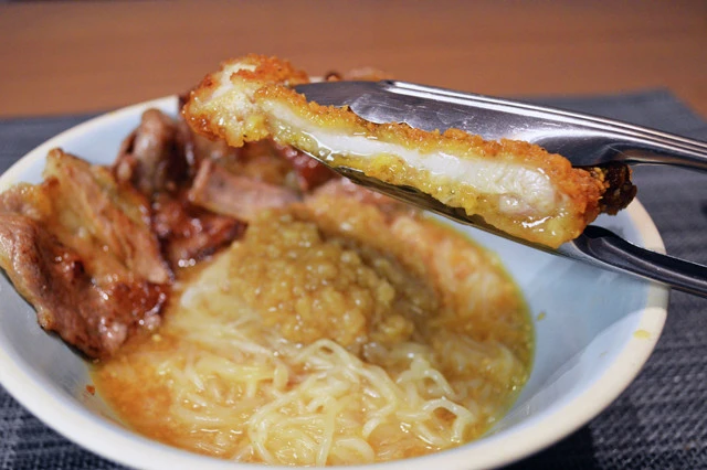 (4)搾る! 仕上げはファミチキを半分に切ったらトングなどを使ってファミチキを搾り、肉汁を垂らしたら完成。3種のアブラマシマシのスタミナ満点ガッツリとうふ麺を堪能せよ!