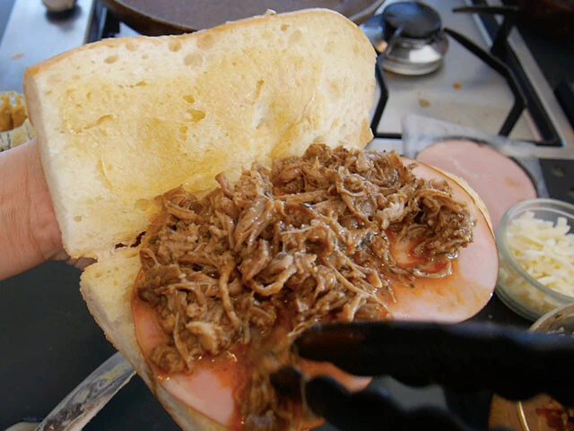 ６．パンの内側にマスタードを塗り、ハム、プルドポーク、チーズ、ピクルスを挟む。