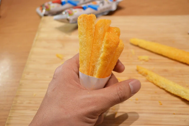 うまい棒チーズ味を縦半分にスライスし、さらに斜めにカットしたら円錐状にした紙筒に挿してアイスのコーン状にする。バニラアイスをのせたら完成。チーズ味＋バニラとコーンの風味が絶品！