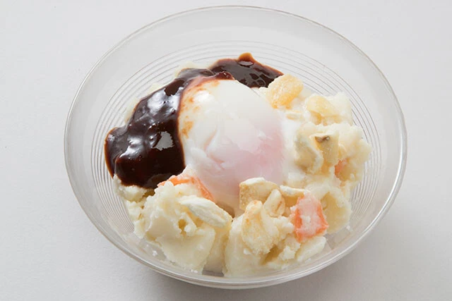 ガッツリとんこつ辛味噌ポテサラ【つまみにんにく＋ポテトサラダ＋温泉卵】①つまみにんにく適量を袋の上からスプーンの背などで叩いて砕く②ポテトサラダに①のにんにくをふりかけ、温泉卵をのせ、とんこつ辛味噌を添える