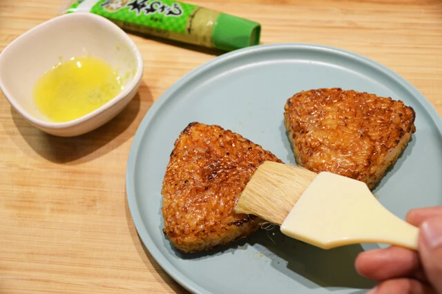 （２）塗る！　温めた焼きおにぎりの両面に溶かしバターをたっぷりと塗ったら、さらにわさびもできる限り多めに塗る。あらかじめバターとわさびを混ぜてから焼きおにぎりに塗ってもよい