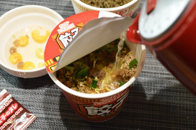 (2)熱湯! カップヌードル 餃子に熱湯を麺全体がギリギリ浸るくらいまで注ぐ。(1)で取り出した謎肉とエビはカップに加えてもいいが、別の食器で湯戻しすると具を均等に包みやすくなる