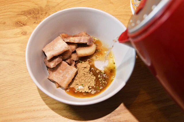 (2)つけ汁! レンチンした「厚切り豚バラ焼き」と、どん兵衛の粉末スープを器に入れ、熱湯を注いでつけ汁を作る。お湯は通常の使用量(410ミリリットル)の半分を目安にしつつ、お好みで調整を