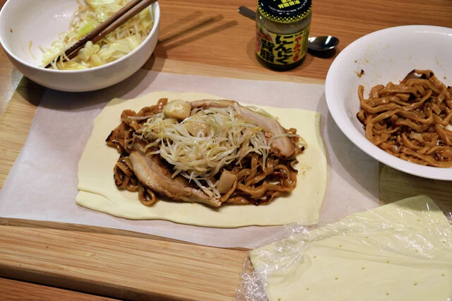 (2)盛る! クッキングシートの上でパイシートを広げ、表面ににんにく背脂をたっぷり塗ったら、その上から麺と具材を盛る。野菜は少なめに、麺を多めにするのがポイント