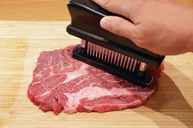 （１）切る！　テンダーライザーを使ってステーキ肉全体の筋を切りながら薄く引きのばしたら半分にカットする。テンダーライザーがない場合は包丁やフォークなどでもある程度は代用可能だ